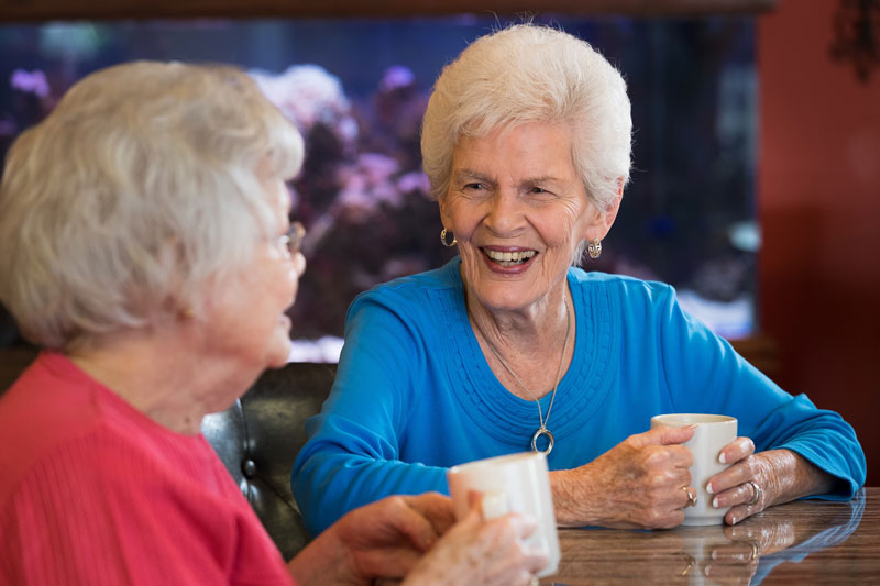 Two ladies are sitting and drinking coffee at the retirement center.t